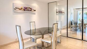 A modern dining area with a glass table and metal chairs, a wall-mounted artwork, and a large mirror reflecting the space.
