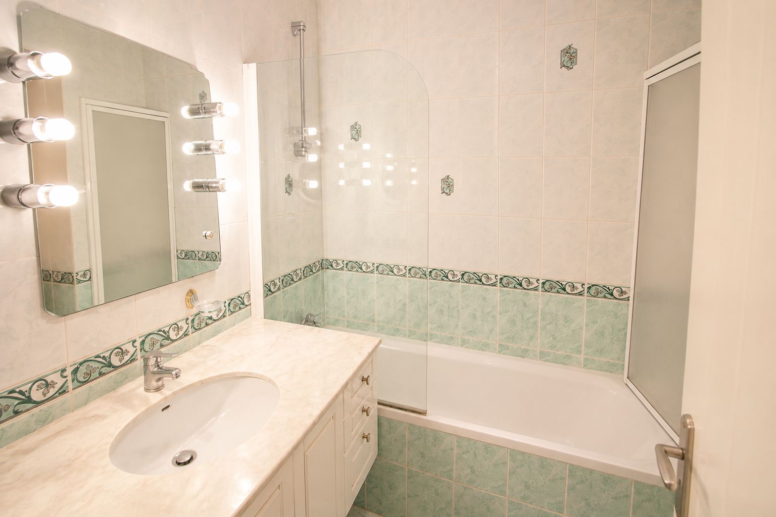A bathroom with a sink, mirror, lights, and a shower.