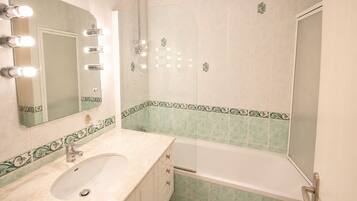 A bathroom with a sink, mirror, lights, and a shower.
