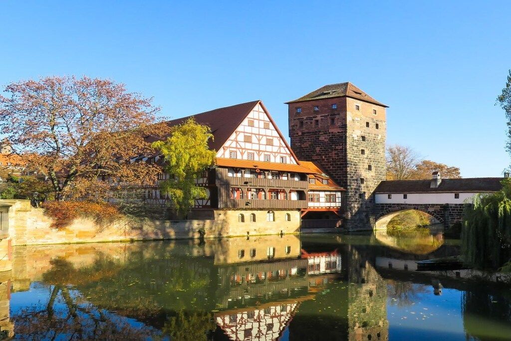 A traditional half-timbered building with a stone tower, reflecting in a calm river.