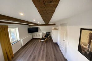 A room with a wooden ceiling, a white radiator, a white door, a black chair, and a television mounted on the wall. - Holiday home in Ellingen with swimming pool (Ellingen)