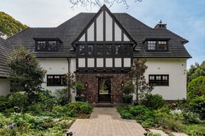 A traditional Tudor-style house with a steeply pitched roof, white exterior walls, and black timber framing. - Sheiling - Heritage Villa with Pool, Sauna & Enchanting Garden (Cape Town)