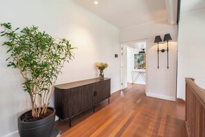 A hallway with a wooden floor, a dark wooden console table, a potted plant, and a painting on the wall. - Sheiling - Heritage Villa with Pool, Sauna & Enchanting Garden (Cape Town)
