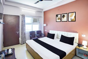 A hotel room with a bed, bedside table, chair, and a window with curtains. - Hotel O BLW Kakarmatta Near Banaras (Varanasi)