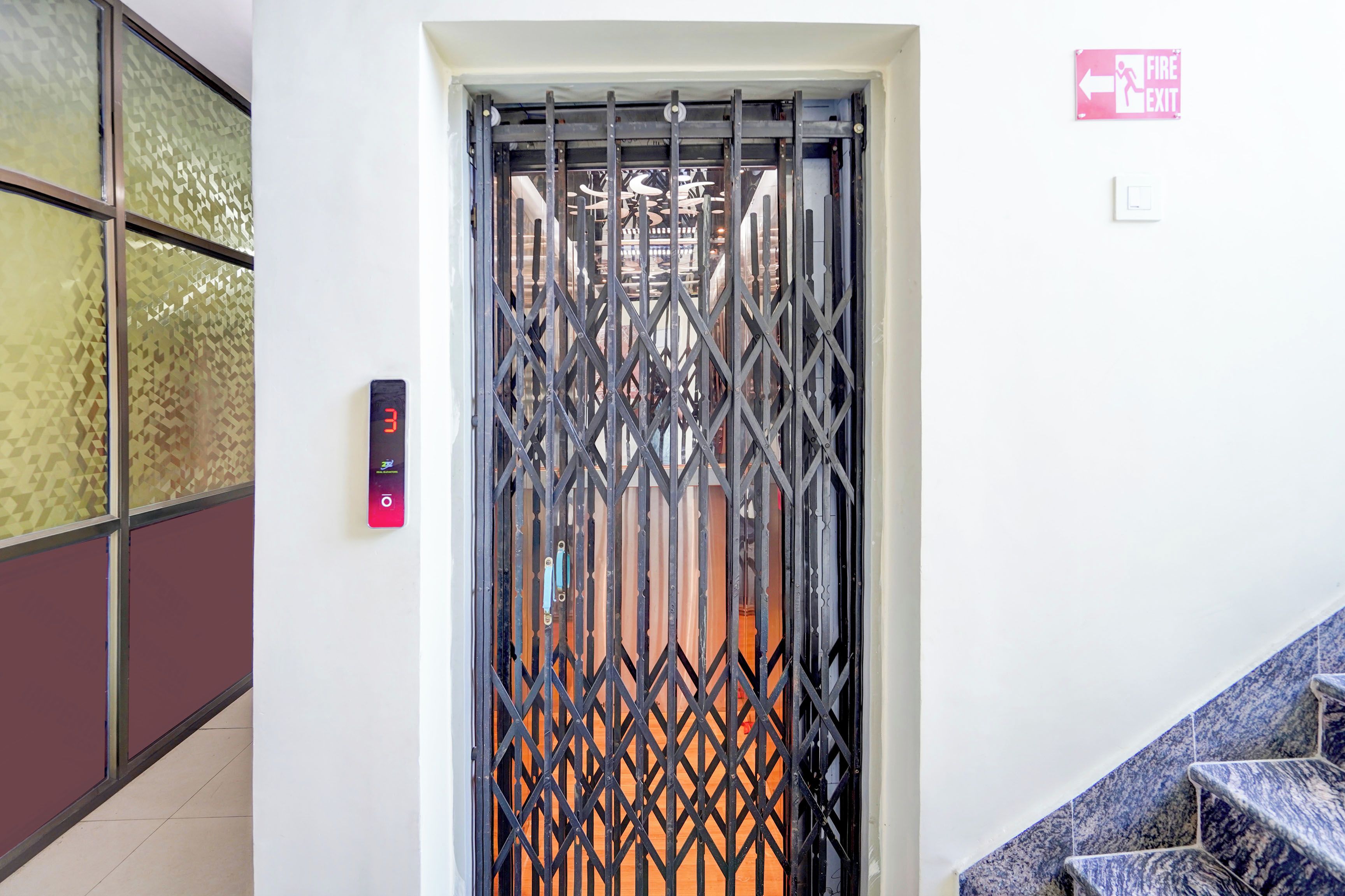Una reja de metal con un candado digital, un letrero de salida de incendios y una escalera con azulejos azules.