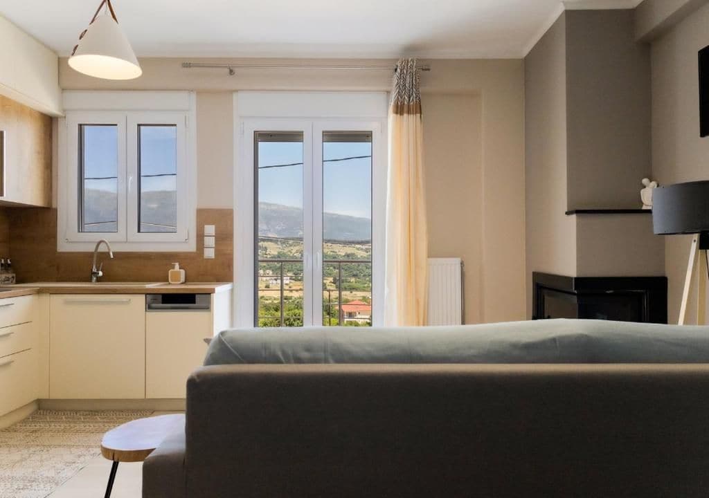 A modern room with a sofa, a small table, a kitchen area, and a view of the outdoors.