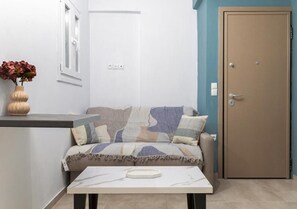 A room with a sofa, a small table, a vase with flowers, a door, and a light switch on the wall.