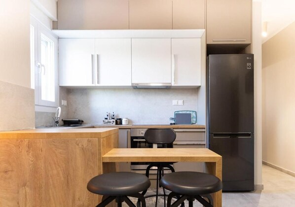 A compact kitchen with white cabinets, a black refrigerator, and a wooden dining table with two stools.