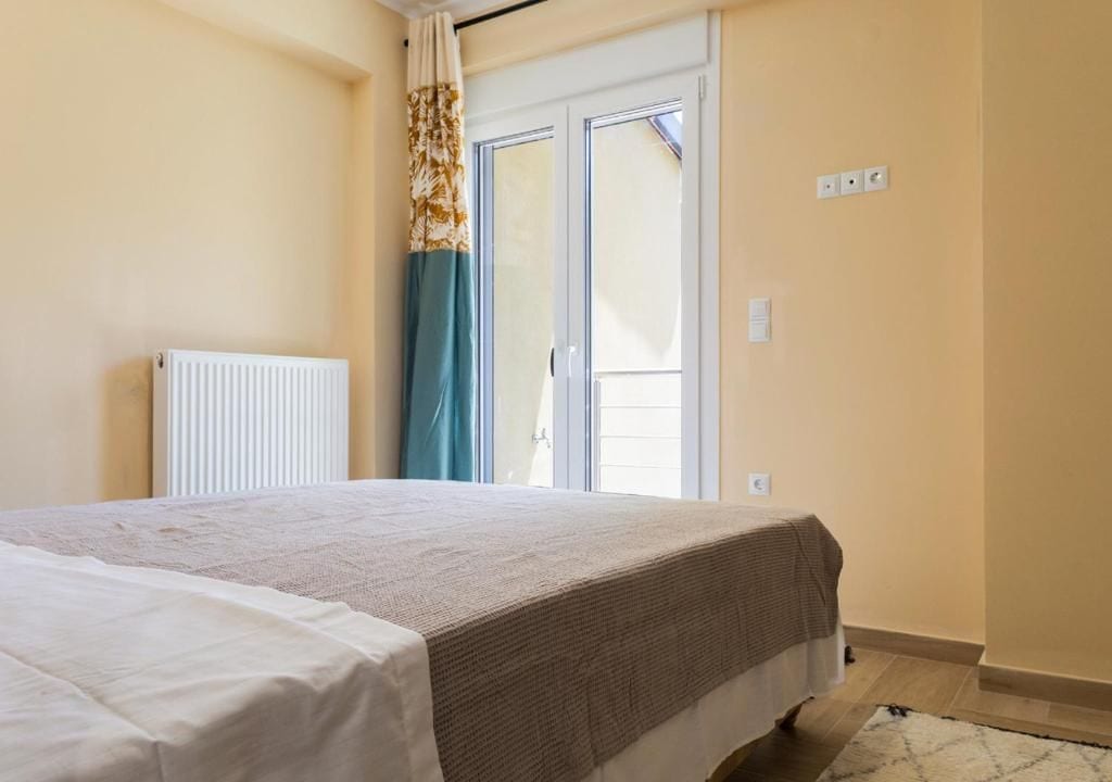 Un dormitorio con cama, radiador, ventana con cortinas y puerta.
