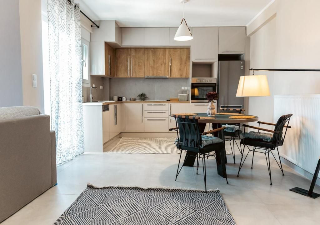 A modern kitchen with a dining area, featuring a central island, pendant lighting, and a view of the living room.