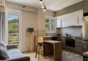 Una cocina moderna con una isla central, una zona de comedor con un sofá y un amplio ventanal con vistas a zonas verdes.