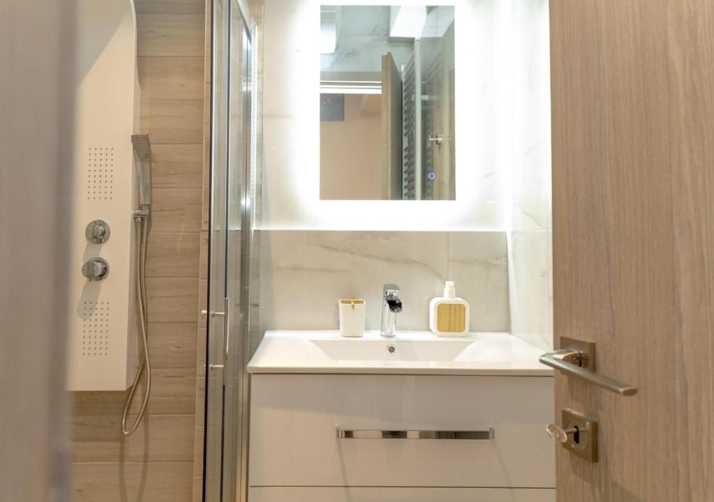 Ein modernes Badezimmer mit einer Duschkabine aus Glas, einem weißen Waschbecken mit Marmorplatte und einem Spiegel darüber.