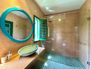 A bathroom with a round mirror, a sink with a green bowl, and a shower with a green door. - HÙA Deluxe 104 (Đà Nẵng)