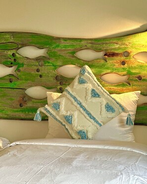 A bed with white bedding and a pillow with a geometric pattern. - HÙA Deluxe 104 (Đà Nẵng)
