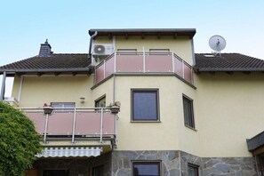 A two-story building with a balcony, a satellite dish, and a stone base. - Holiday home with 4 bedrooms (Ochtendung)