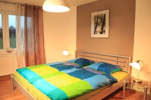 Une chambre à coucher avec un lit, deux lampes de chevet, une fenêtre avec des rideaux et un tableau encadré au mur.