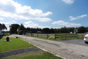 Ein Kiesweg führt zu einem umzäunten Bereich, in dessen Nähe ein Auto geparkt ist.
