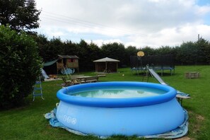 Ein Garten mit einem blauen aufblasbaren Pool, einer Rutsche, einem Pavillon und einem Basketballkorb.