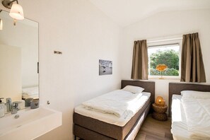 A hotel room with a bed, a bedside table with a lamp, a window with curtains, a mirror, and a bathroom with a sink and toiletries. - Holiday home in Ballum with swimming pool (Ballum)