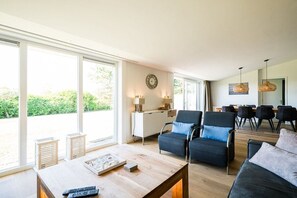 A modern living room with a wooden coffee table, two armchairs, a sofa, and a dining area with chairs. - Holiday home in Ballum with swimming pool (Ballum)