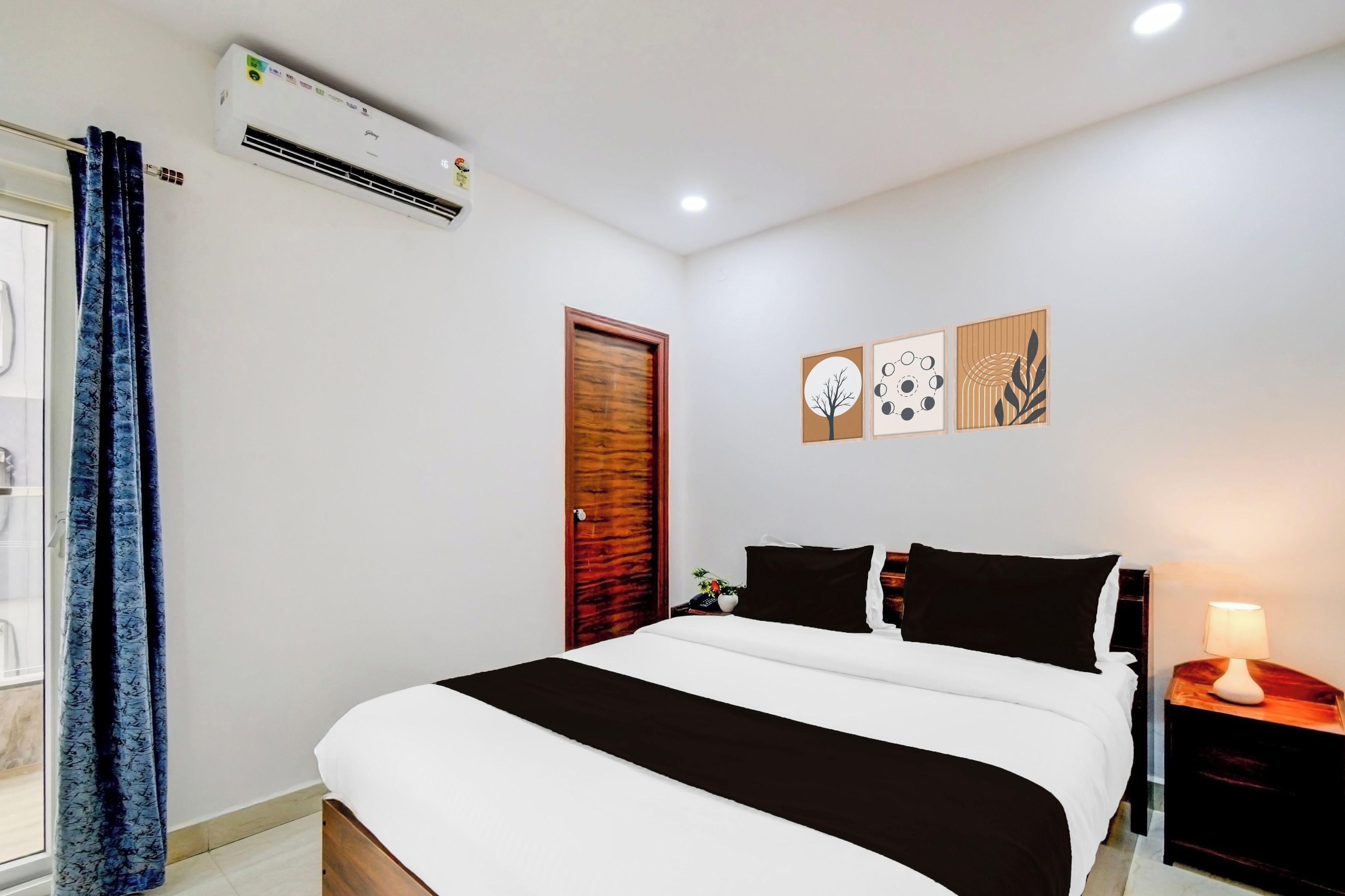 A bedroom with a bed, a bedside table with a lamp, a wall-mounted air conditioner, and a door.