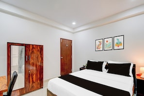A bedroom with a bed, a wooden wardrobe, a desk, and a chair. There are three framed artworks on the wall. - Super Townhouse Nallagandla Nest  (Hyderabad)