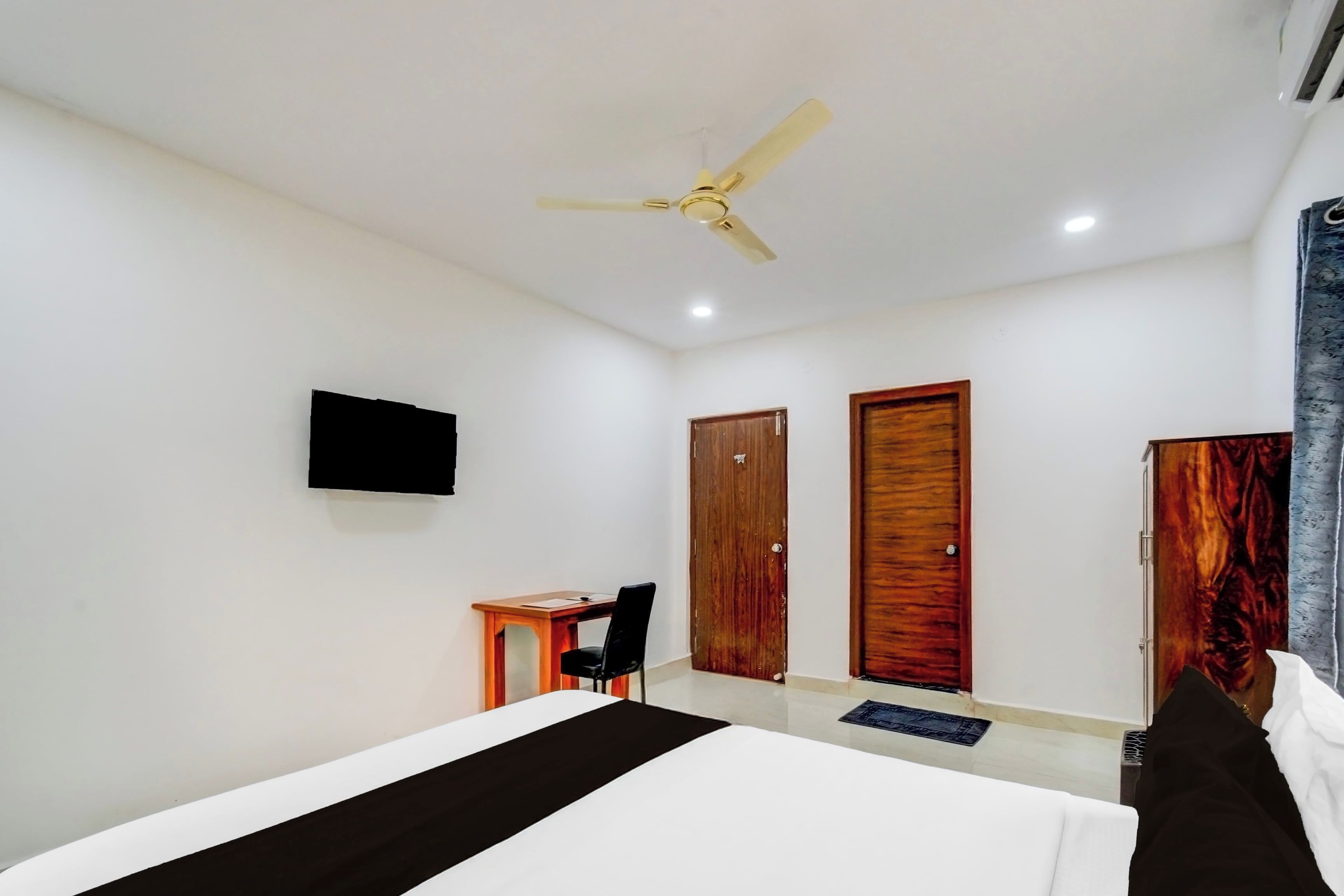 Un dormitorio con cama, escritorio, silla, televisor y dos puertas.