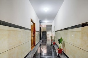 Un pasillo con una puerta de madera, plantas en macetas y una escalera que lleva a otra zona.
