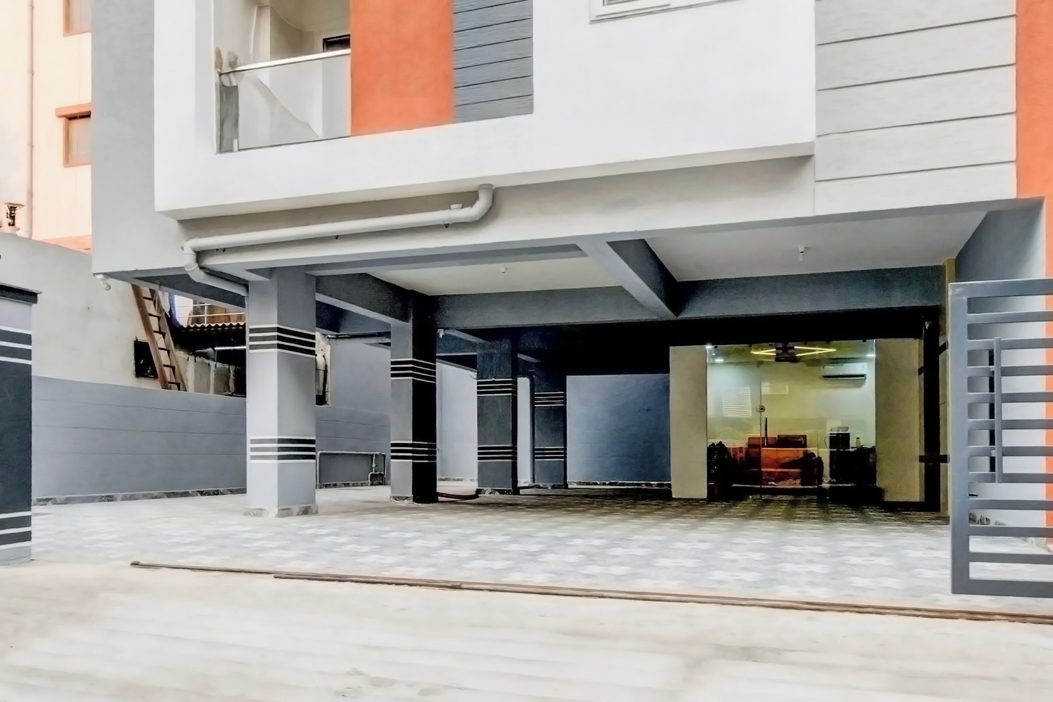 Un immeuble résidentiel moderne doté d’une entrée abritée, de colonnes structurelles apparentes et d’une allée d’accès fermée par un portail.