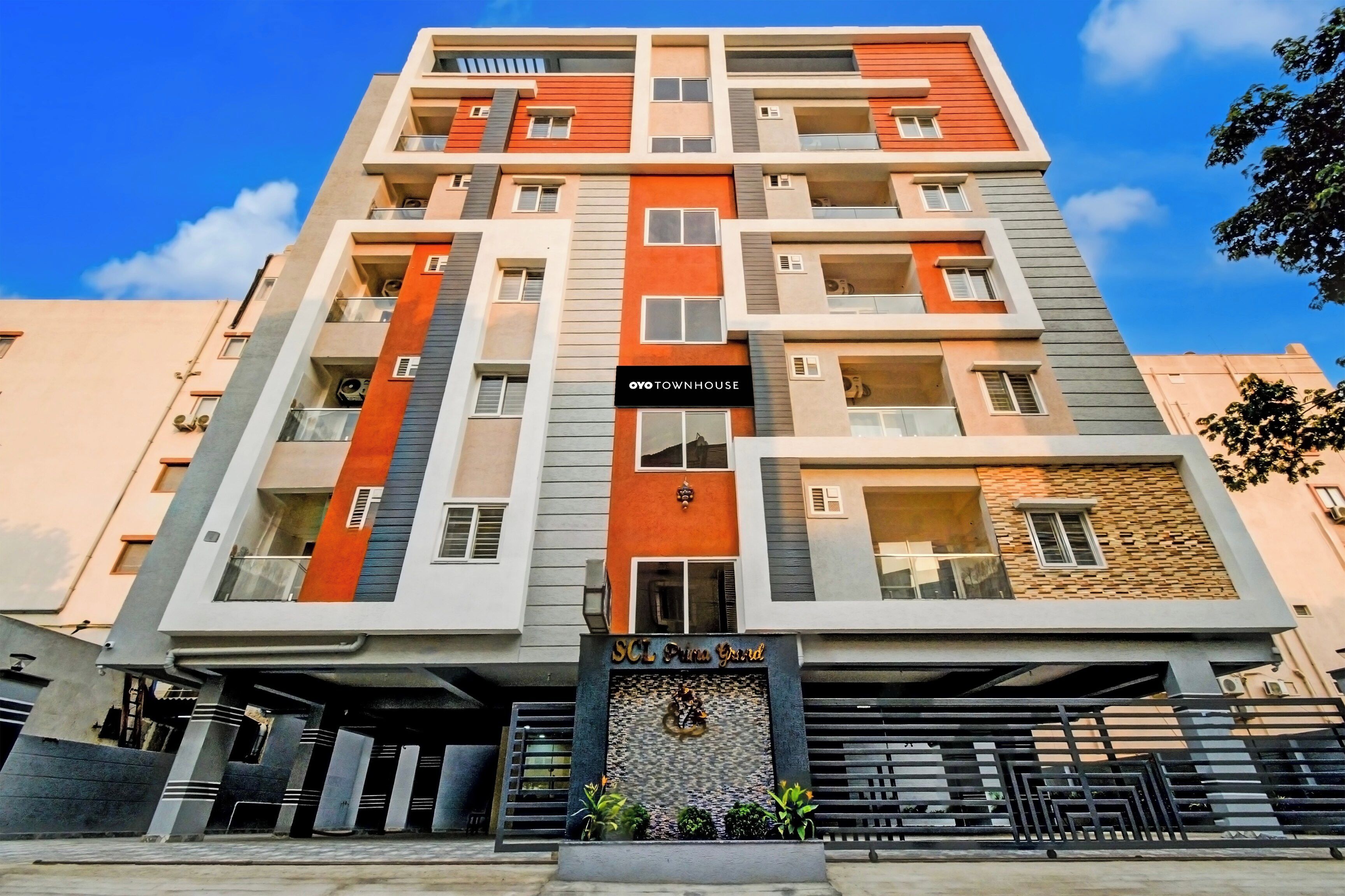 Un immeuble à plusieurs étages doté de balcons, une enseigne indiquant « OYO TOWNHOUSE » et une entrée marquée « SCL Prima Grand ».