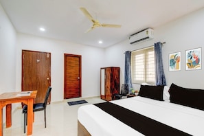 A hotel room with a bed, a desk, a chair, a ceiling fan, an air conditioning unit, and two framed artworks on the wall. - Super Townhouse Nallagandla Nest  (Hyderabad)