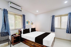 A hotel room with a bed, a nightstand, a chair, and two windows with curtains. - Super Townhouse Nallagandla Nest  (Hyderabad)