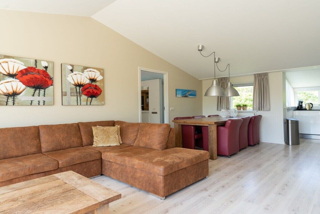A modern living room with a sectional sofa, a wooden coffee table, and a dining area with red chairs.