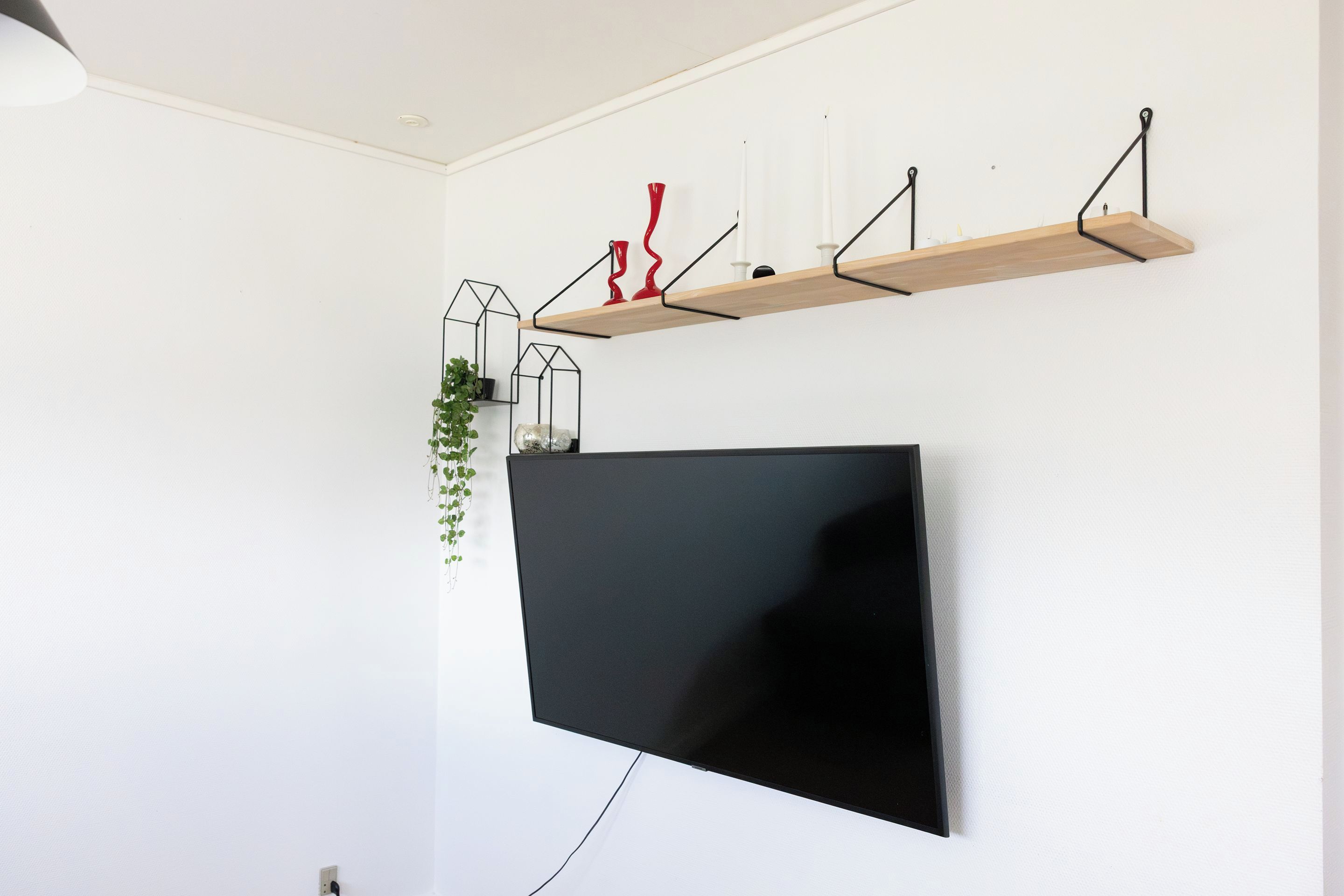 Una TV a schermo piatto montata a parete, con uno scaffale in legno sopra che contiene oggetti decorativi.