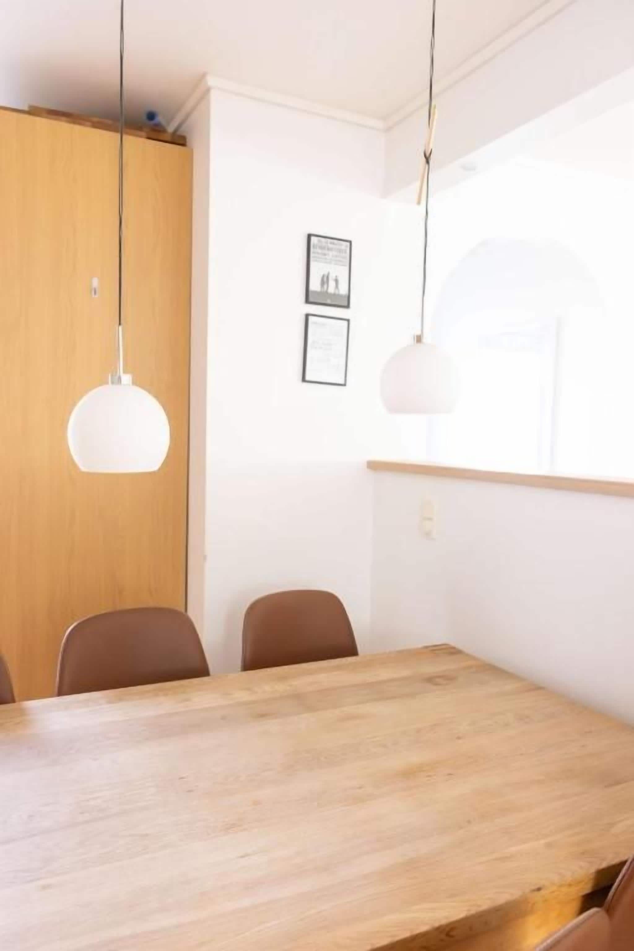 Uma área de refeições com mesa e cadeiras de madeira, luminárias pendentes e quadros nas paredes.
