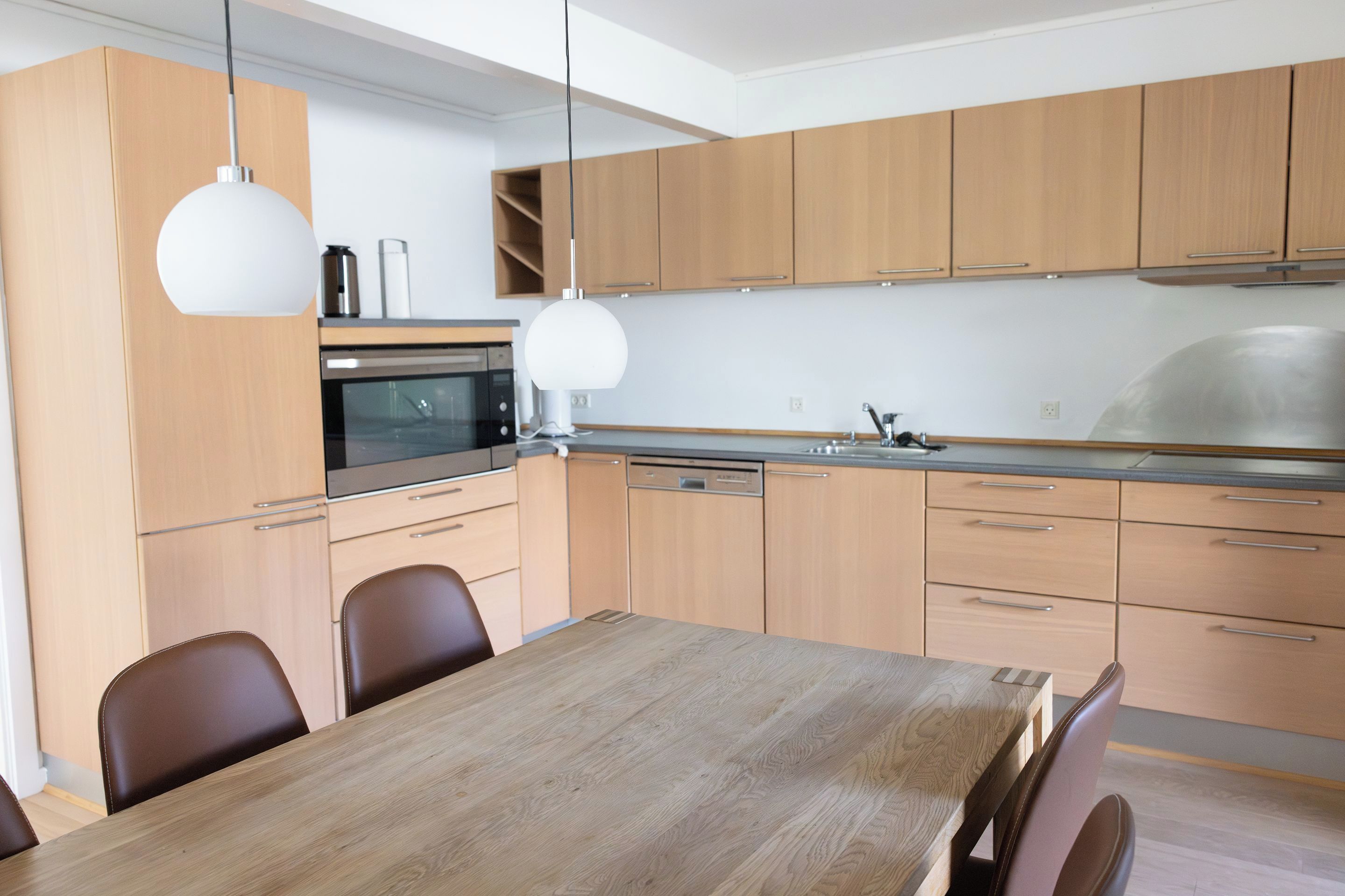 Una cucina moderna con mobili in legno, un lavandino in acciaio inossidabile e un tavolo da pranzo con sedie.