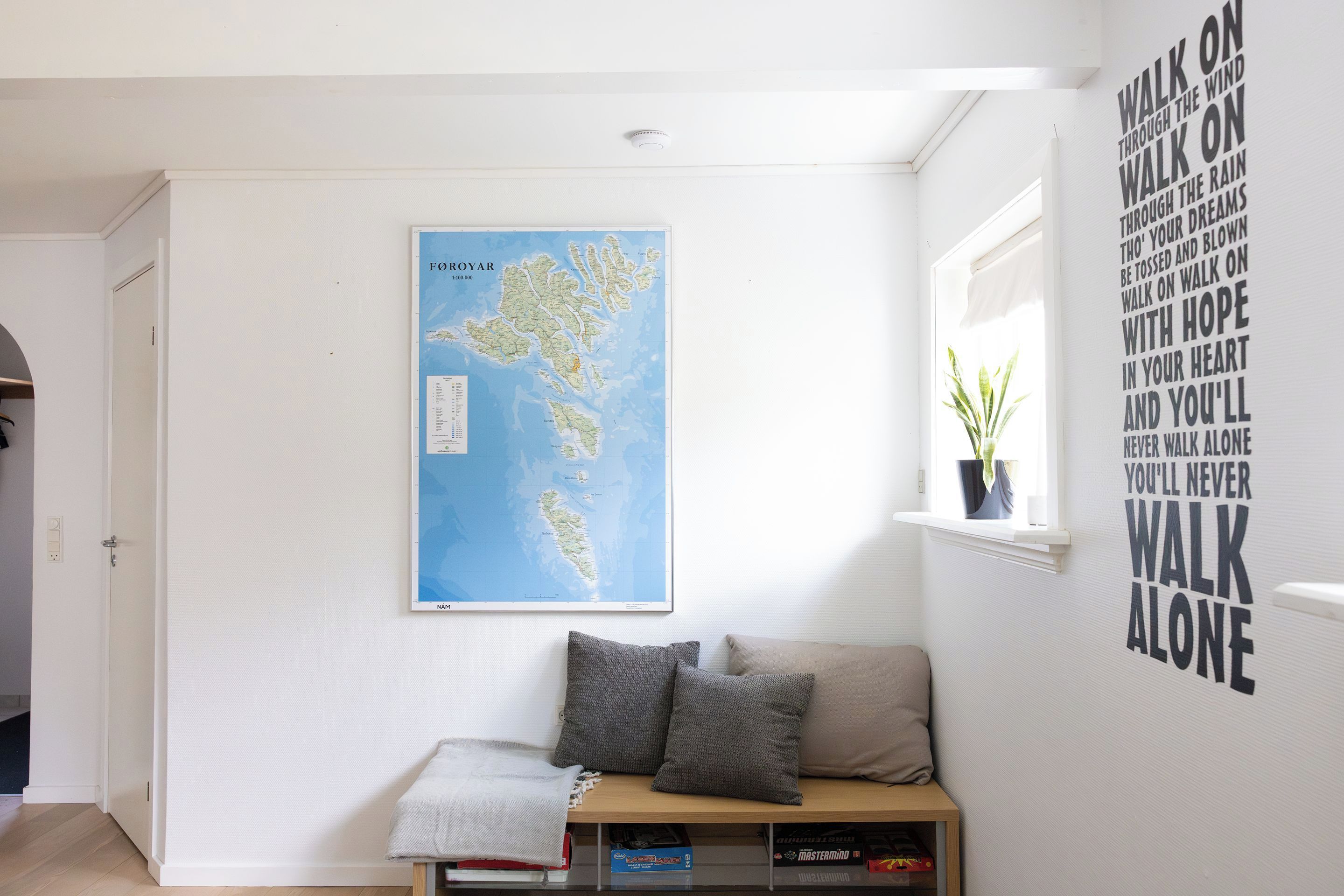 A room with a map of Foyroyar on the wall, a window with a plant, and a bookshelf with books.