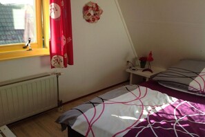 Et soveværelse med et vindue, en radiator og en seng med et mønstret sengetæppe.