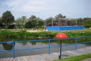 A park with a playground, a wooden deck, and a body of water. - Holiday home with 2 bedrooms (Den Helder)