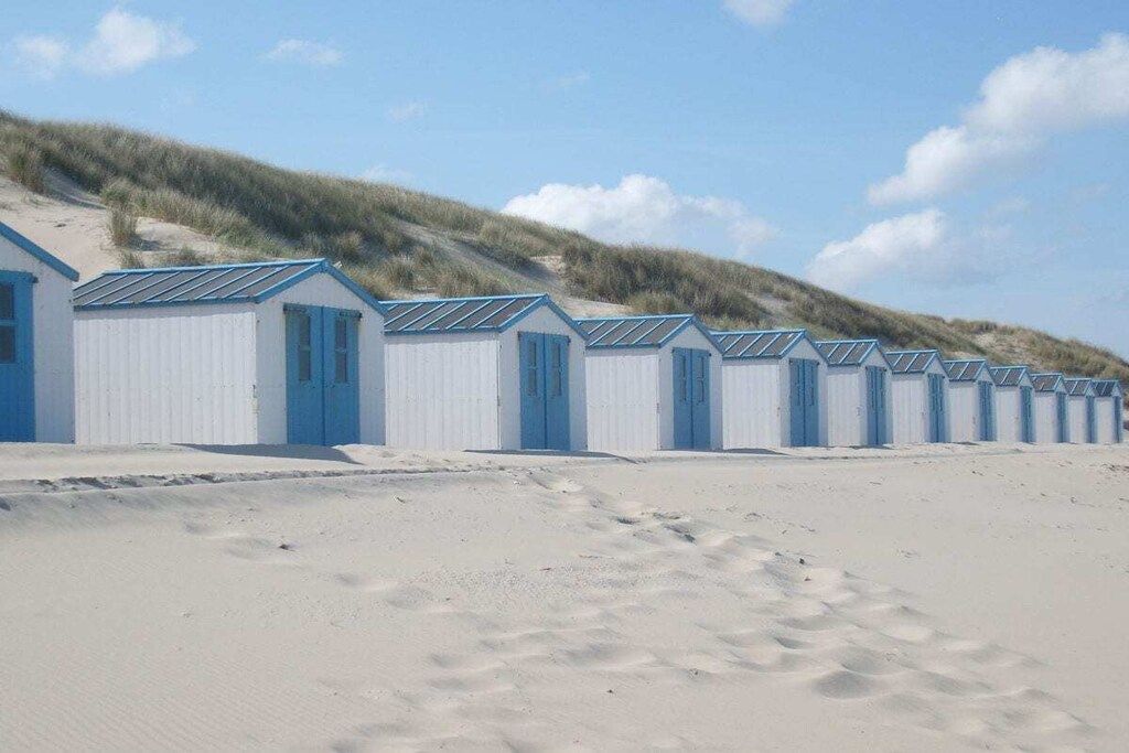 Una hilera de cabañas de playa, con arena al frente y dunas en el fondo.