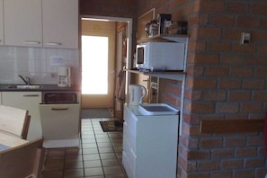 Een compacte keuken met witte apparaten, een spoelbak en een deur naar een andere kamer.