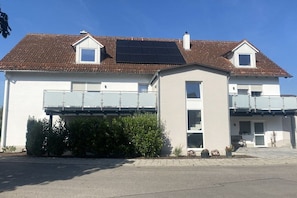 A two-story house with a solar panel on the roof, a covered balcony, and a small garden area. - in the Zum Inn apartment building (Bad Füssing)