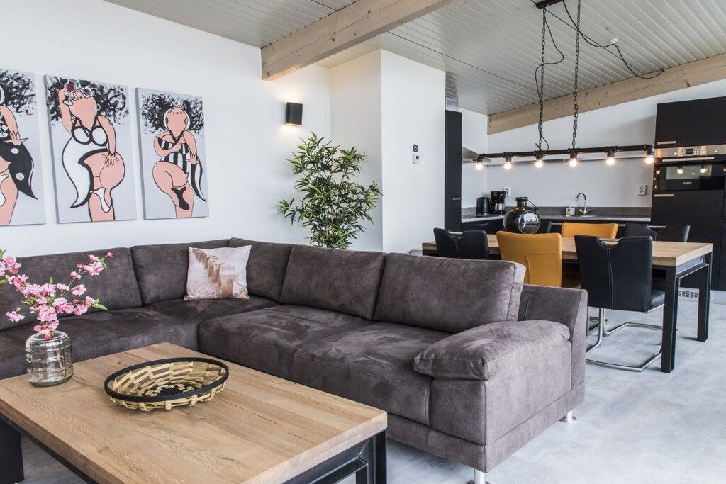 Un salon moderne avec un canapé gris, une table basse en bois et un coin repas comprenant une table noire et des chaises jaunes.