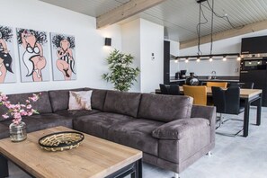Ein modernes Wohnzimmer mit einem grauen Sofa, einem Holztisch und einem Essbereich mit einem schwarzen Tisch und gelben Stühlen.