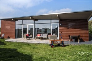 Ein modernes Haus mit einer Terrasse, Gartenmöbeln und einem Wagen mit der Aufschrift 'ROOTS'.
