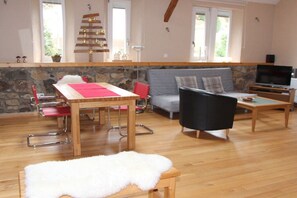 A living room with a wooden table, a sofa, a TV, and a stone wall. - Farmhouse in Bachstrasse (Kelberg-Zermüllen)