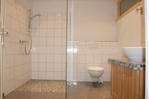 Une salle de bain avec douche, toilettes et un lavabo doté d’un plan de travail carrelé.