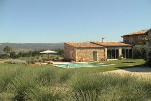 Une maison en pierre avec une piscine, entourée de pelouse et sous un ciel dégagé.