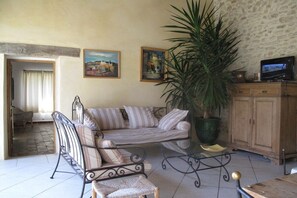 A living room with a sofa, armchair, and a large potted plant. There are paintings on the wall and a television on a cabinet. - with private pool in the Luberon - 223 ROU (Roussillon)