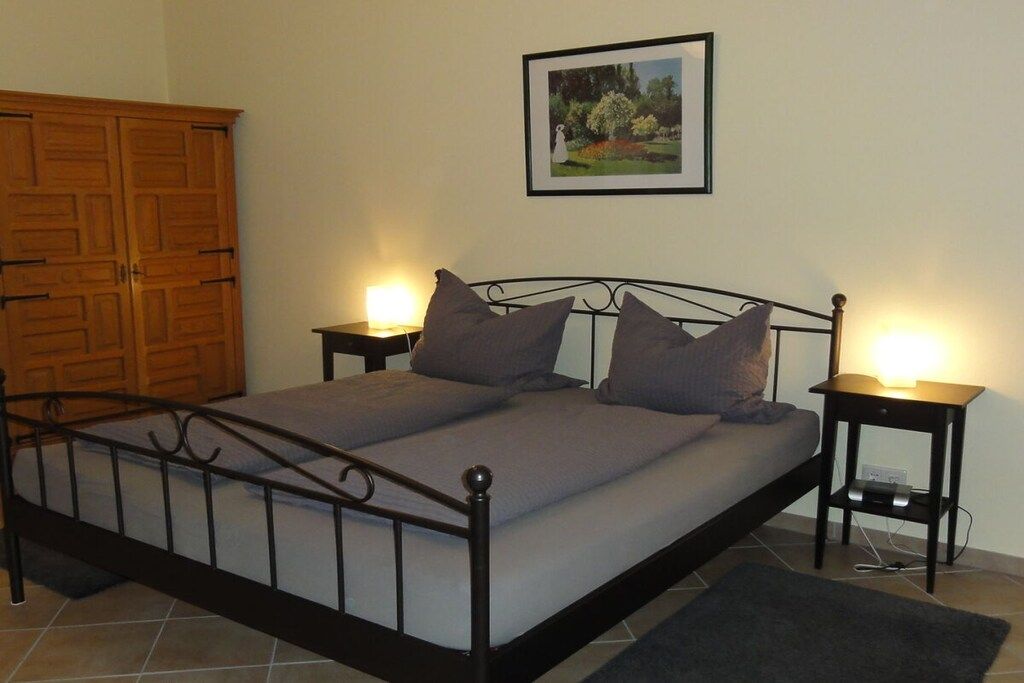 Una camera da letto con una struttura letto in metallo, due comodini con lampade, un armadio in legno e un quadro appeso al muro.
